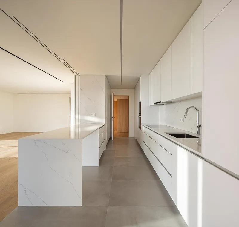 Galley kitchen with white cabinetry, marble island, and grey tile floor beneath recessed track lighting