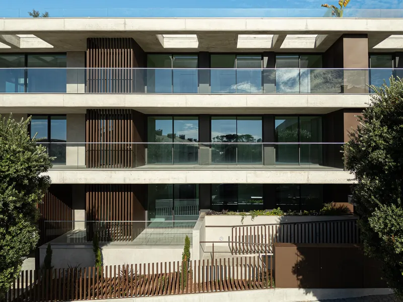 Street facade showing stacked balconies with glass railings and vertical timber screens flanked by mature trees