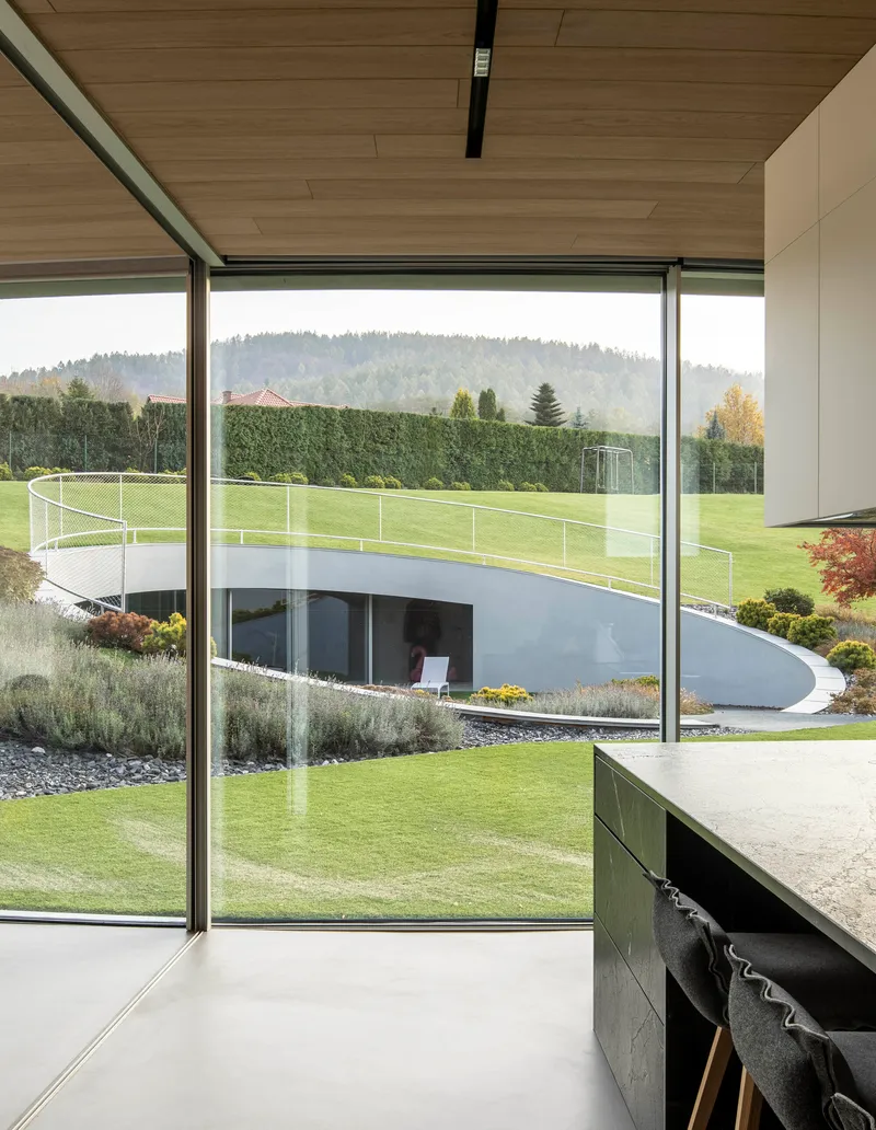 Floor-to-ceiling glazing framing the curved rooftop terrace and planted beds beyond the timber ceiling