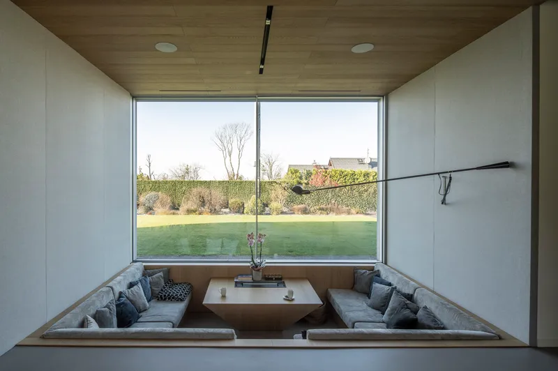Sunken seating pit with upholstered benches framed by timber and glass walls overlooking the lawn