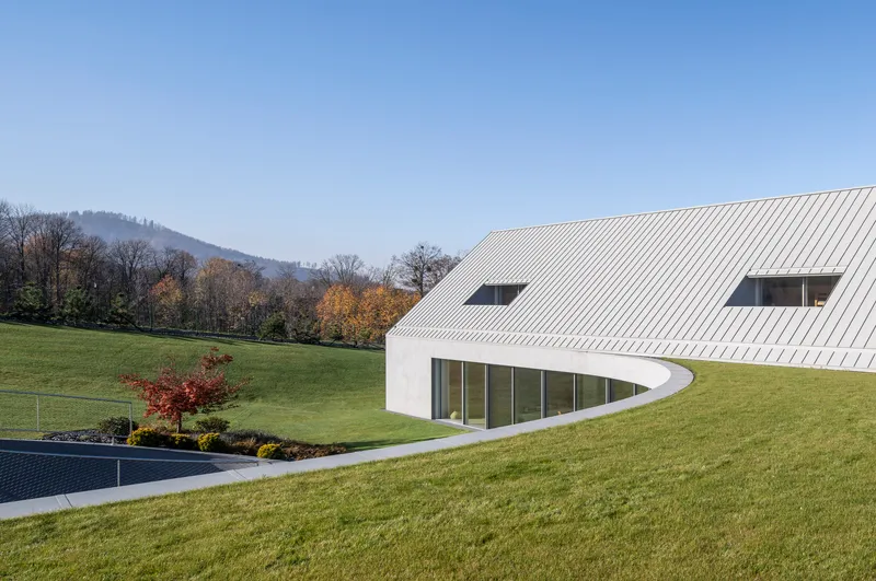 Ribbed metal roof sweeping down to glass walls that curve into the sloping hillside in autumn