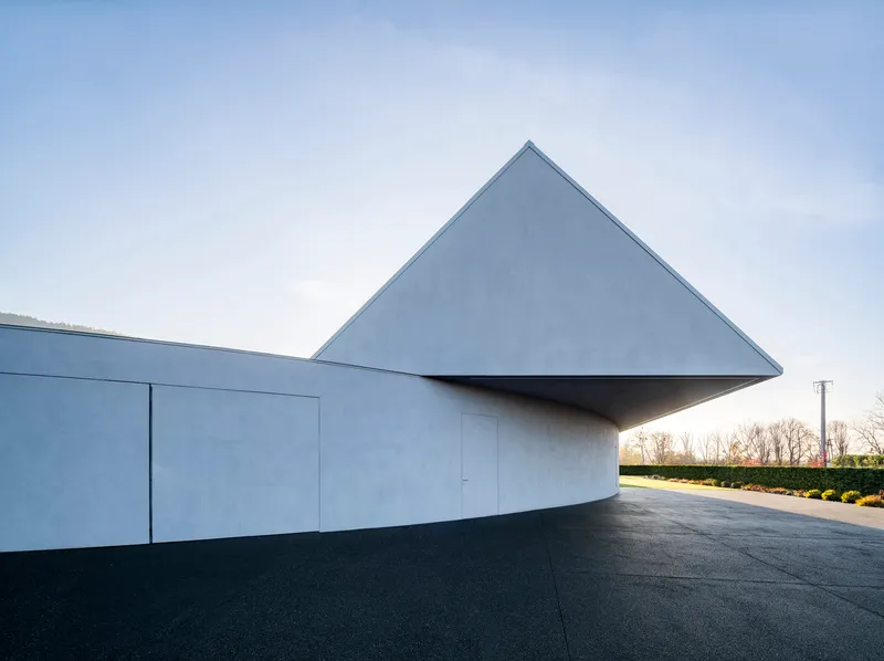 Cantilevered triangular roof volume hovering over the curved white base at dusk