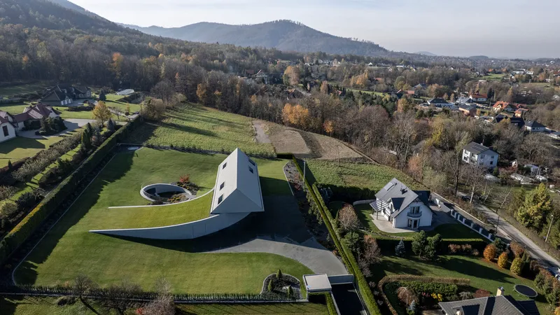 Aerial view showing white gabled house with curved underground extension in terraced landscape