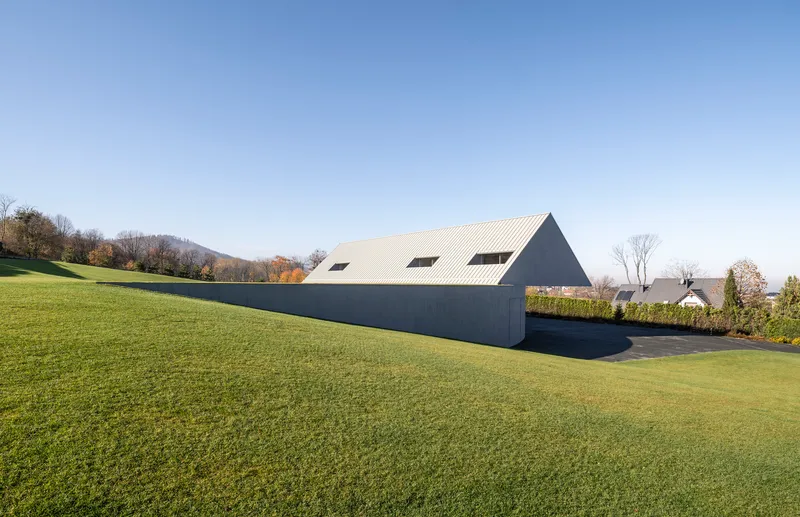 Side elevation showing the ribbed metal roof and dark facade against rolling hills in autumn