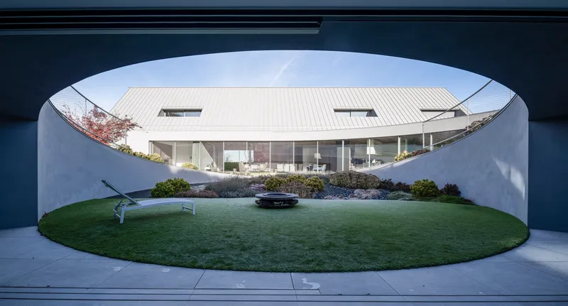 View through arched concrete portal onto glass-walled living space and circular lawn courtyard below