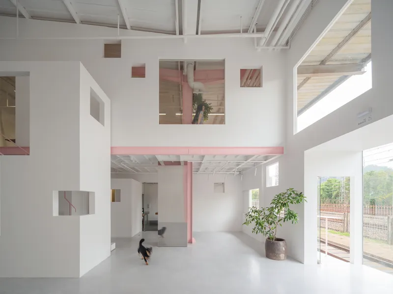 Mezzanine level with pink steel walkway connecting white volumes as a person sits below