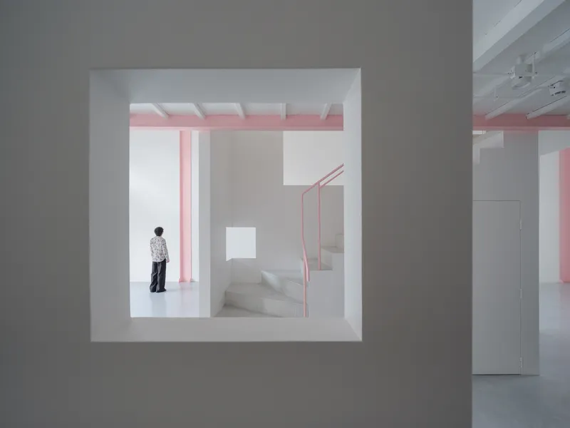 View through a square wall opening showing a person standing near pink steel stairs