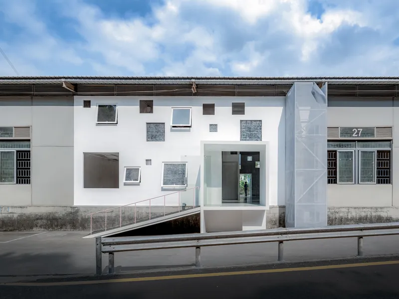 Street view of white facade with scattered windows and recessed entrance under cloudy sky