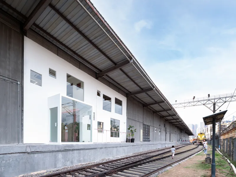 White inserted volume with large glazed opening beneath corrugated metal canopy along railway tracks