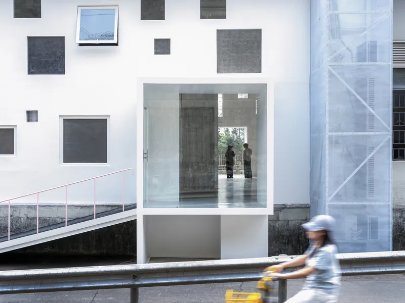 Recessed entrance with glass vestibule and scattered window openings as motorcyclist passes by