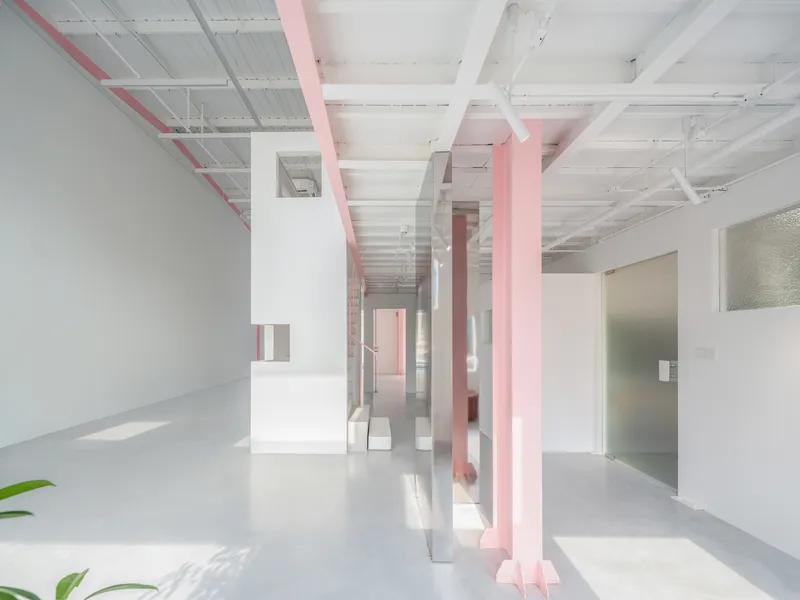 Interior view with pink structural columns and white partition walls beneath translucent corrugated ceiling