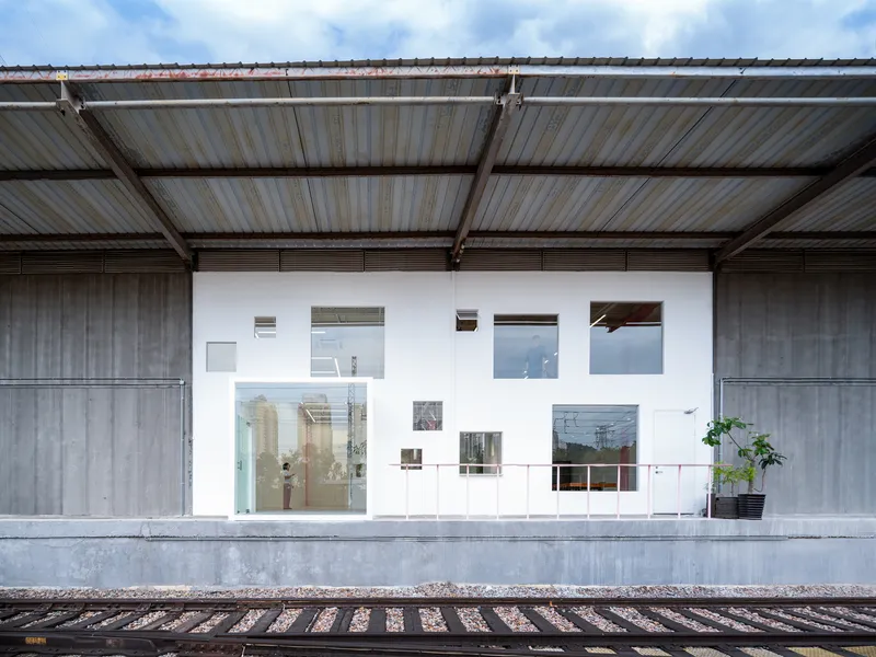 White facade with varied window openings and potted plant viewed from railway platform