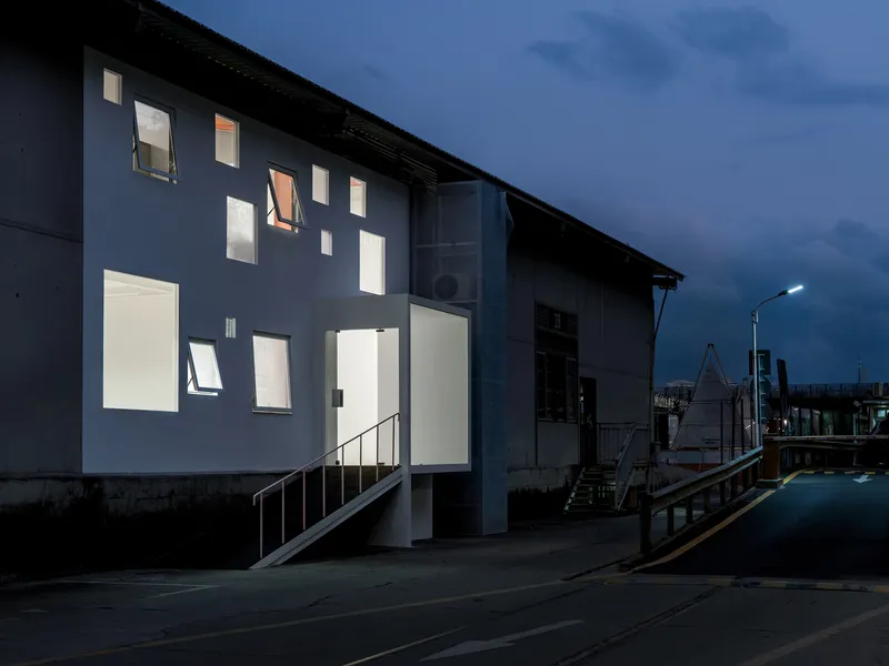 Street facade with scattered windows glowing warmly at dusk beside an exterior metal stair