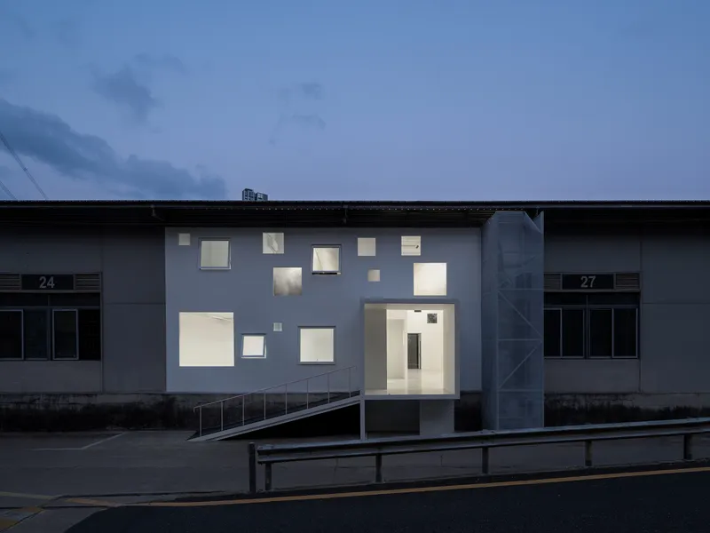 Front elevation showing irregular window openings illuminated against a dark blue evening sky
