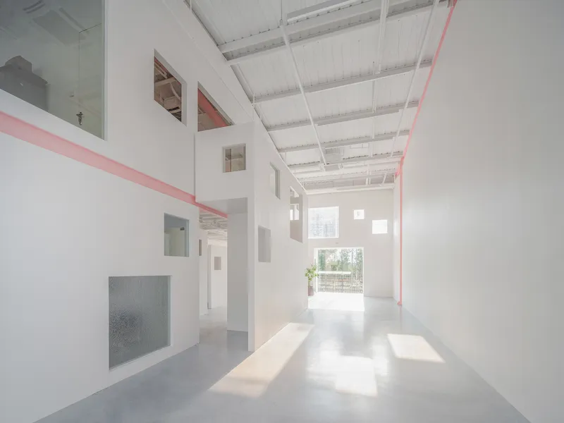 Double-height interior hall with white walls, exposed ceiling joists and pink steel beams