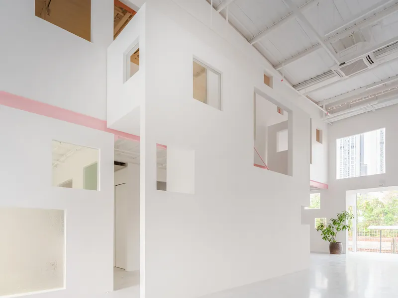 White interior partition with cut-out openings and pink steel trim beneath a sawtooth skylight