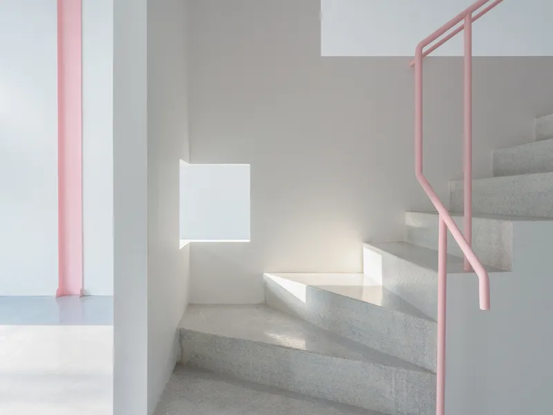 Terrazzo staircase with pink tubular handrail and sunlight casting shadows on white walls