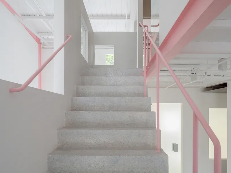 View up the concrete stairs framed by pink tubular railings under a white slatted ceiling