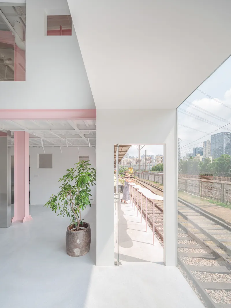 Interior opening to an exterior balcony overlooking railway tracks with a potted tree in foreground