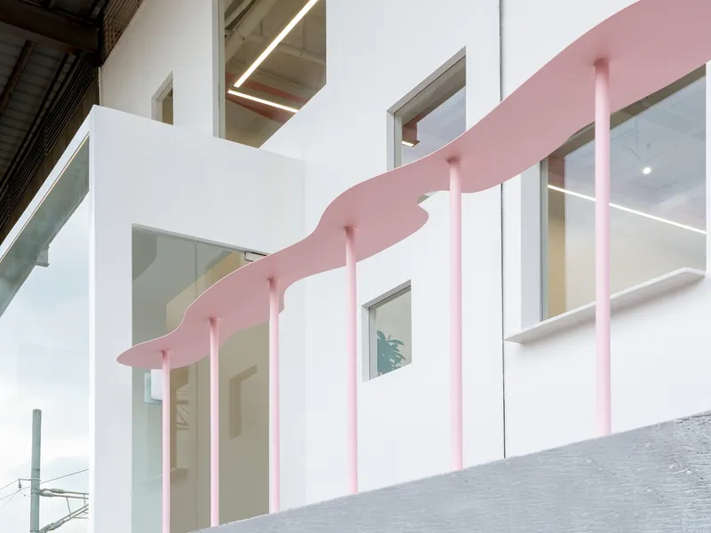 White facade with irregularly placed windows and a pink undulating canopy supported by pink columns