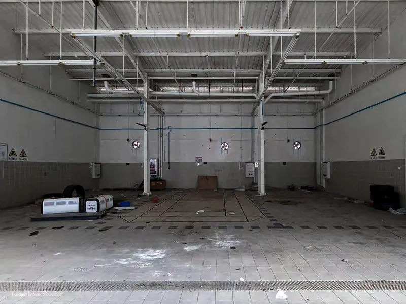 Interior of a garage bay with exposed ceiling ducts and wet concrete floor
