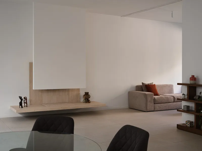 Open-plan living space with floating travertine hearth, white plastered fireplace hood, and pale timber flooring