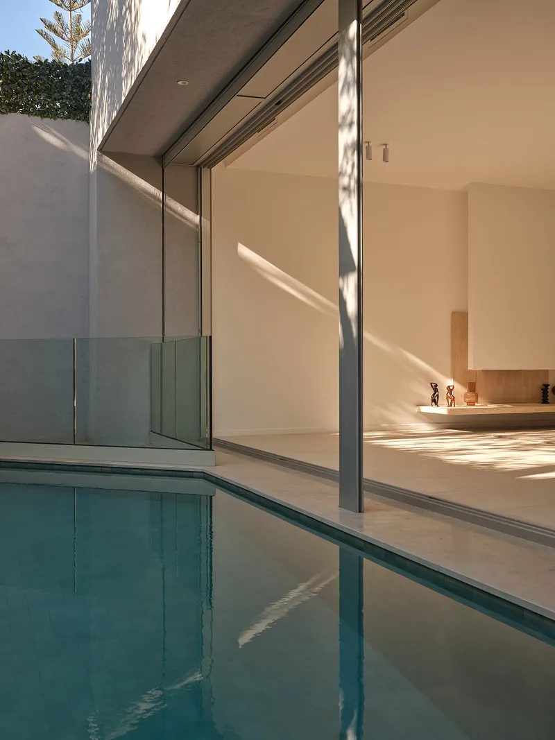 Swimming pool reflecting floor-to-ceiling glass doors and concrete soffit with dappled tree shadows
