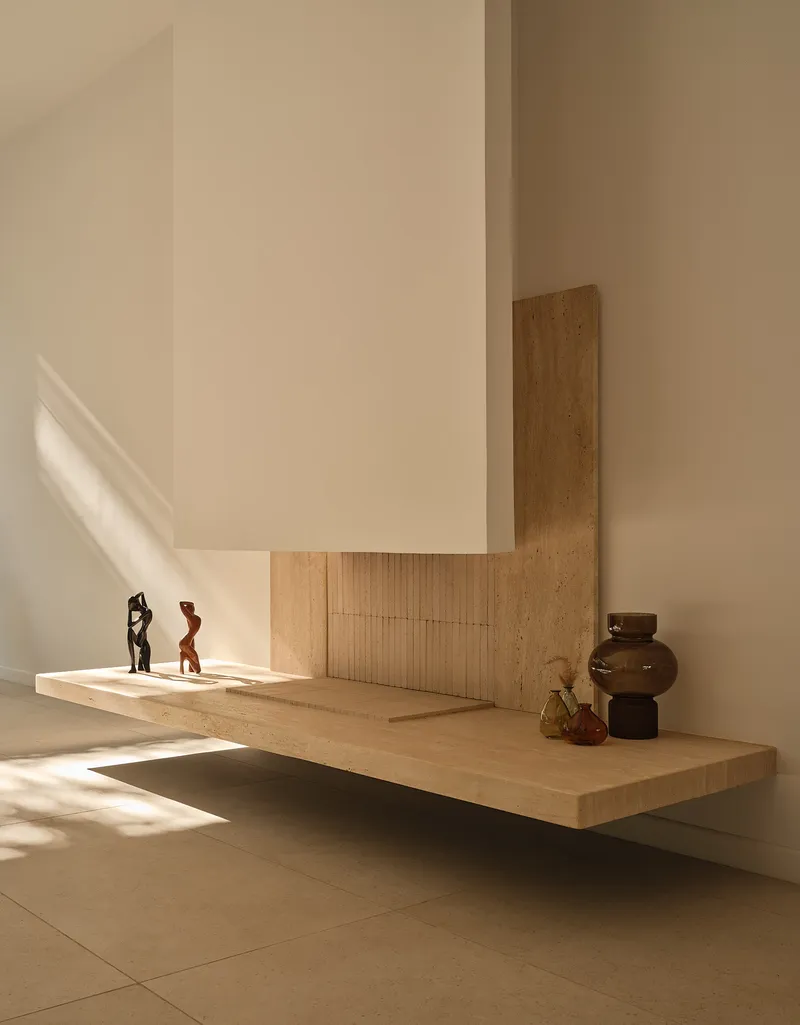 Floating timber shelf with sculptural objects catching angular afternoon sunlight on pale walls
