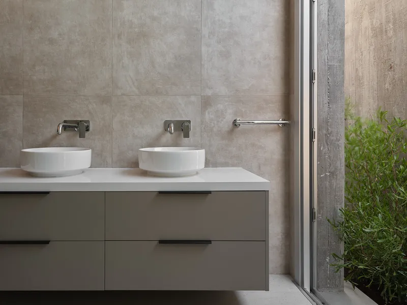 Double vessel sinks on a floating vanity beside a glazed door opening to a planted courtyard