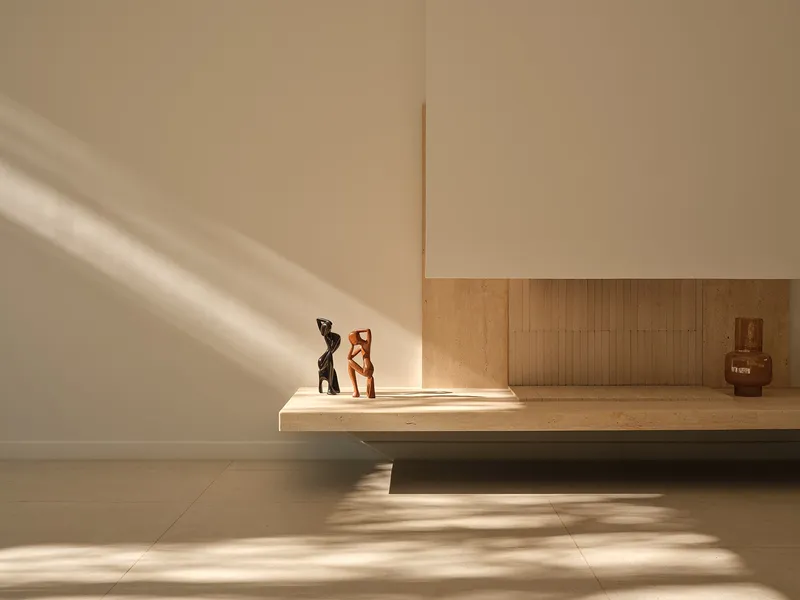 Low timber bench with sculptures lit by angular afternoon sunlight across pale floor tiles