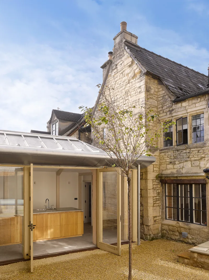 Courtyard showing the glazed extension with timber cabinetry opening onto gravel with a young tree