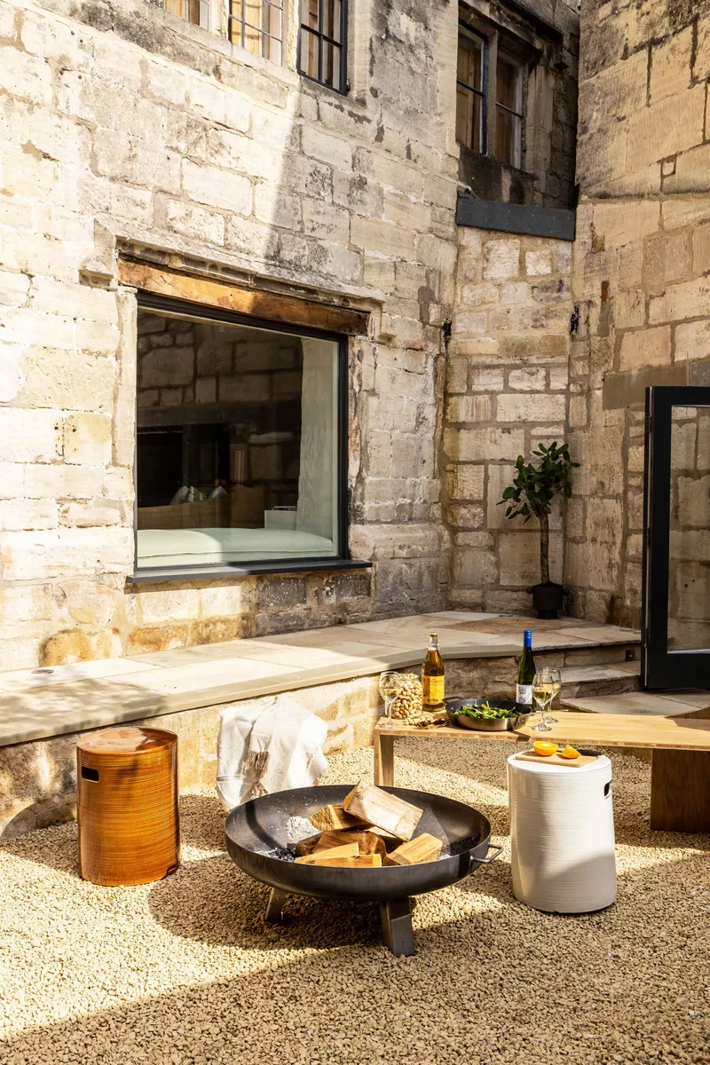 Outdoor terrace with fire bowl and seating framed by weathered stone walls in afternoon sunlight