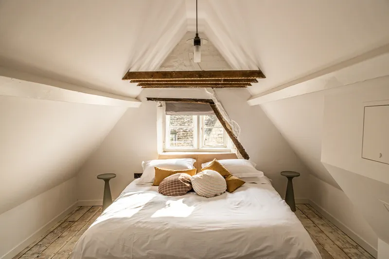Attic bedroom with exposed timber beam and white plastered sloped ceiling lit by a dormer window