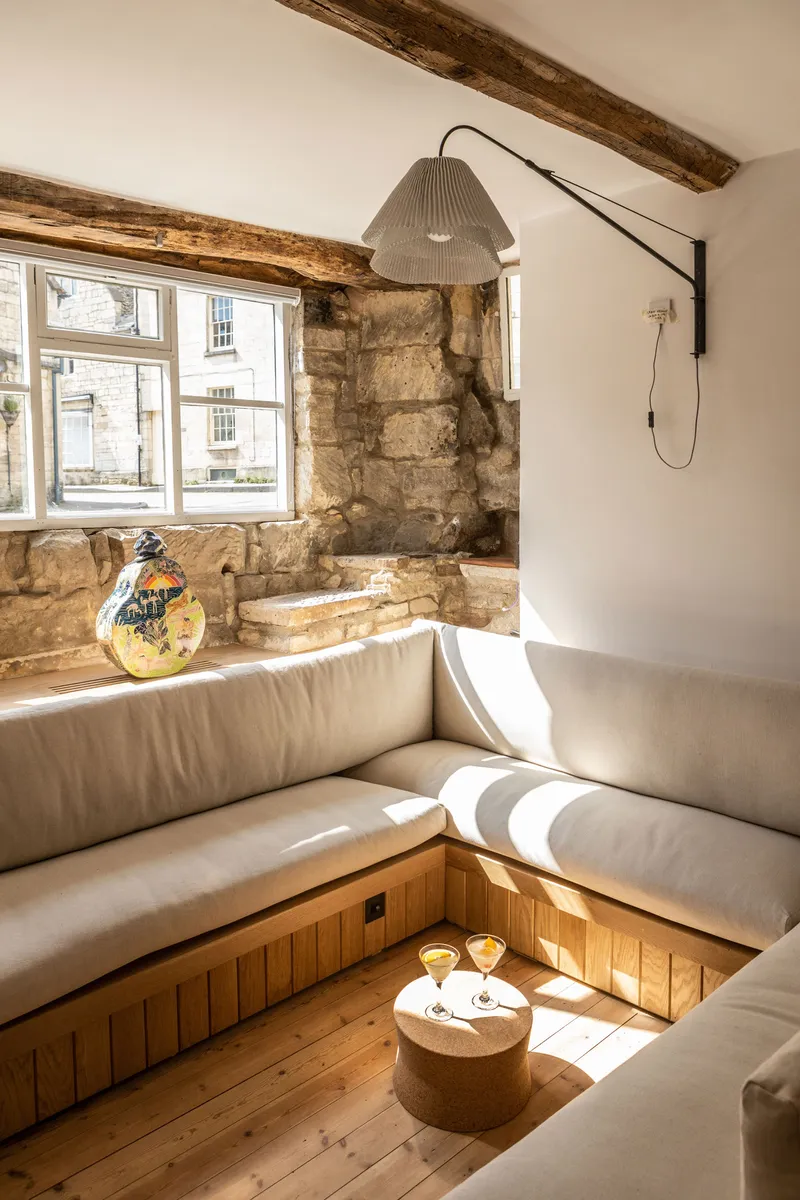 Sunken seating area with upholstered benches and exposed timber beams beside a window overlooking the street
