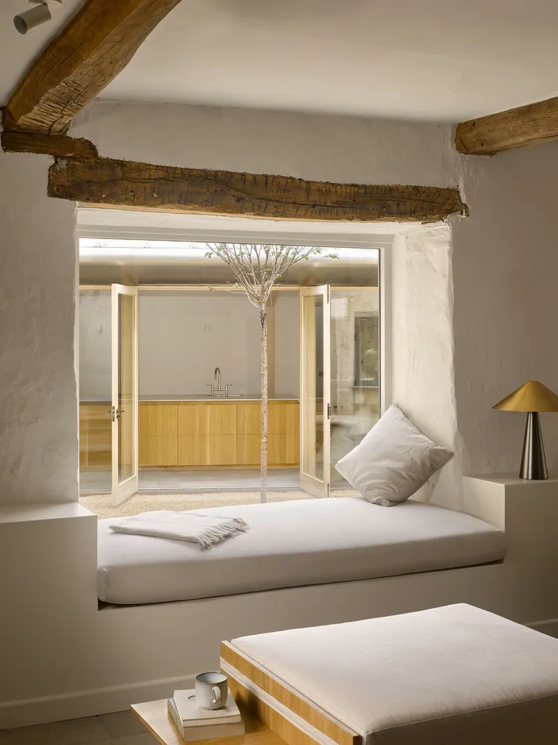 Built-in window seat beneath exposed timber lintel framing a view into the courtyard with a tree