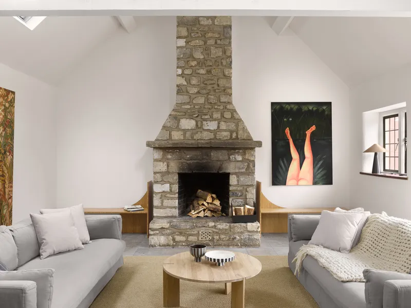 Stone fireplace with stacked firewood flanked by timber benches beneath a white vaulted ceiling with skylights