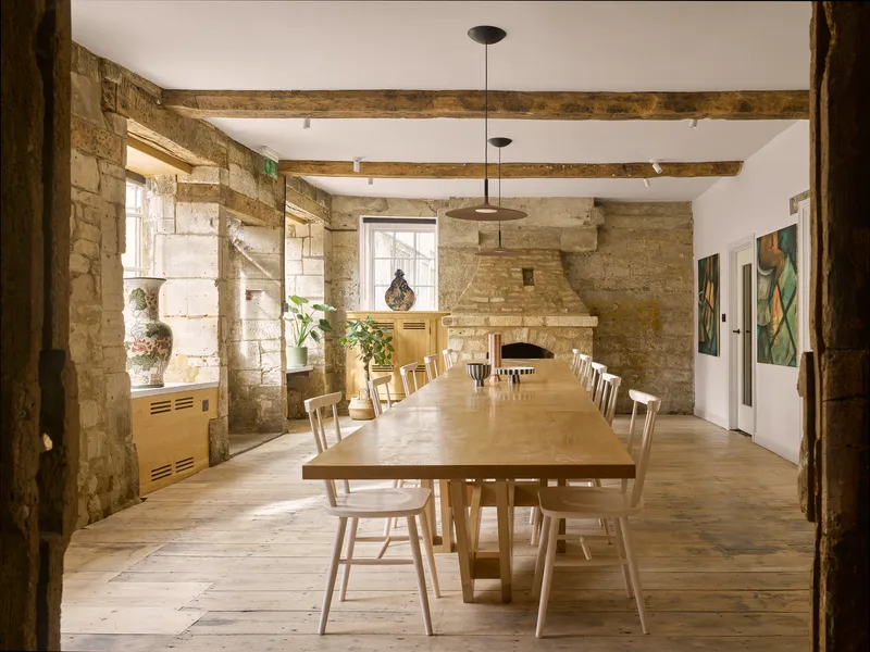 Long communal table with wooden chairs in a dining room with exposed stone walls and timber beams