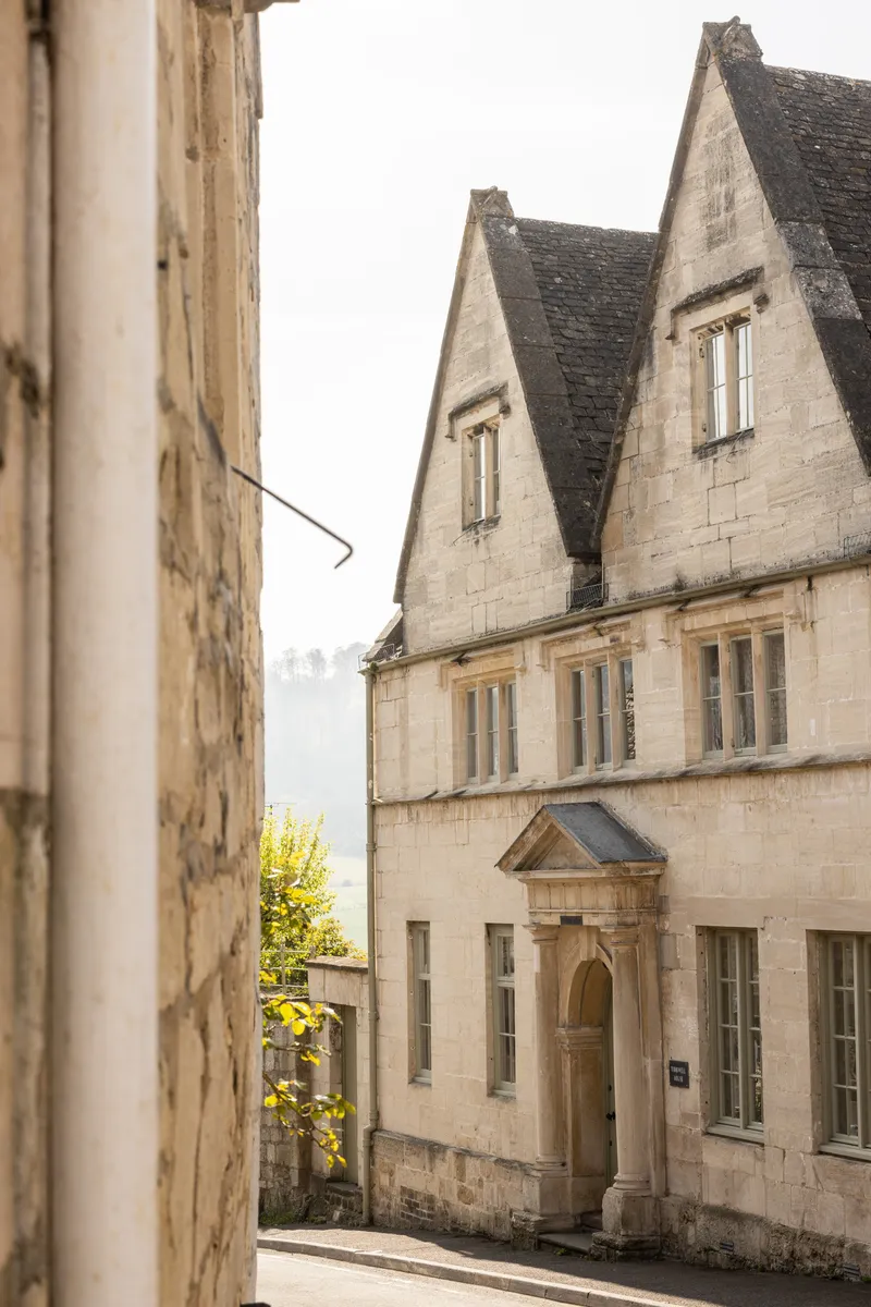 Street view of the limestone facade with twin gables and arched entrance on an overcast day