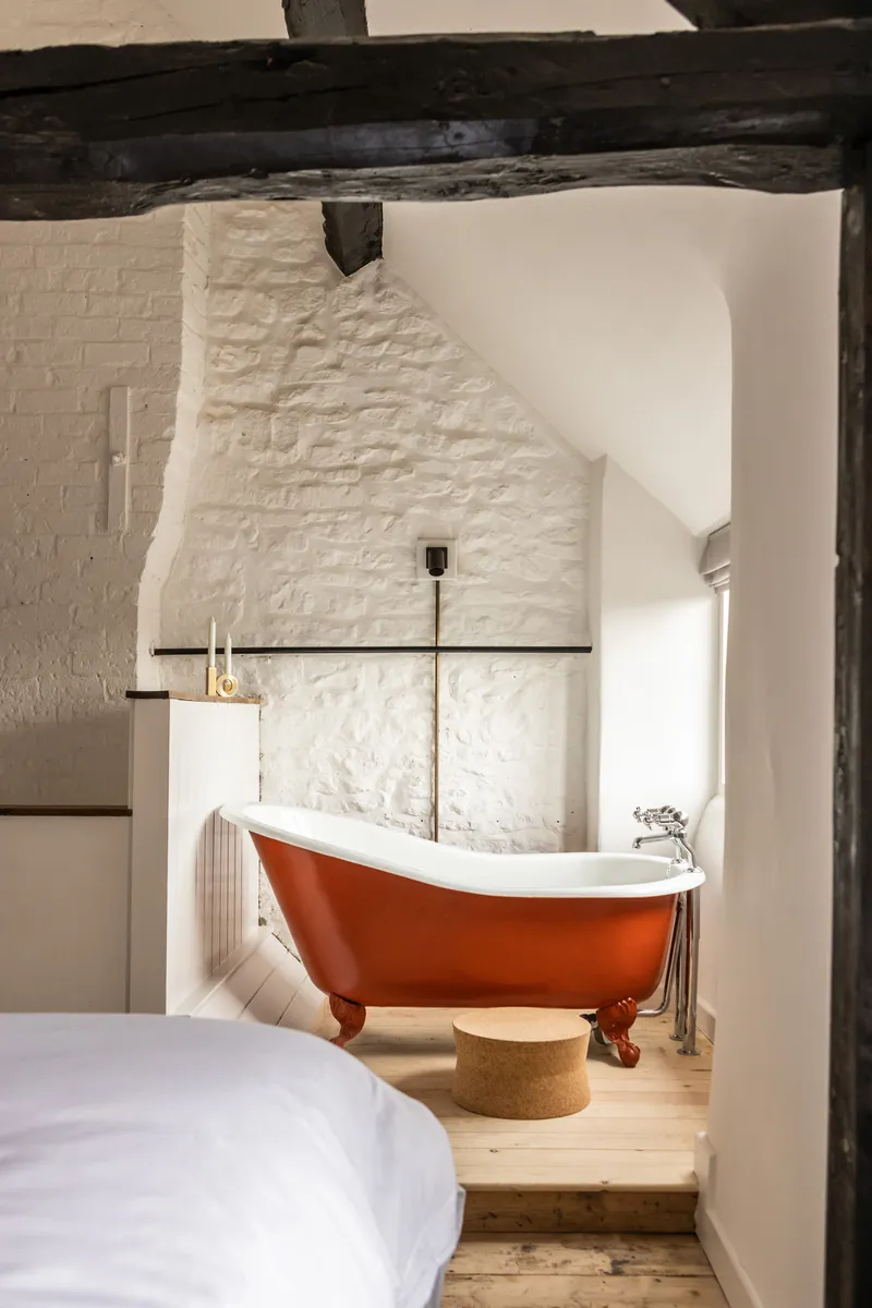 White painted brick bathroom alcove with exposed timber beams and orange clawfoot tub on timber flooring
