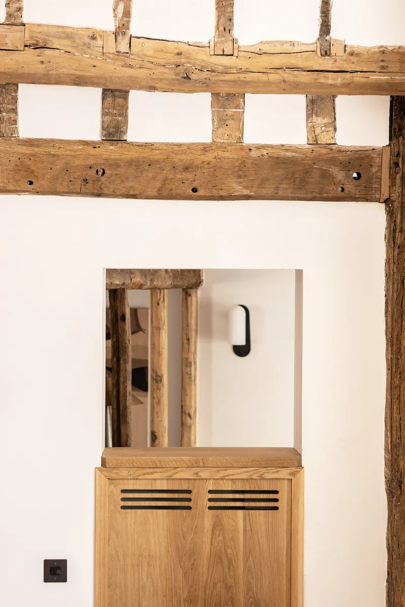 Timber frame infill wall with white plaster and recessed opening revealing oak cabinet below exposed beams