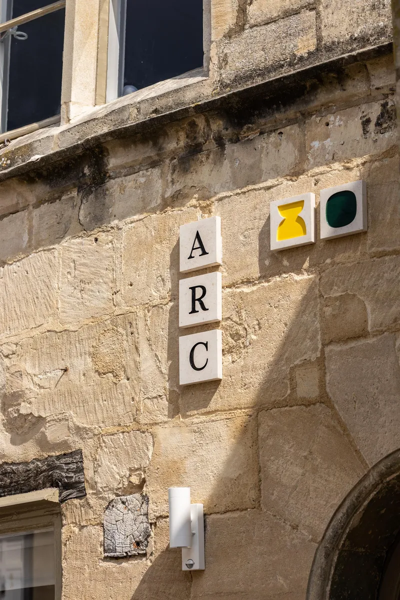 Vertical signage tiles mounted on weathered limestone wall beneath a window in afternoon sunlight