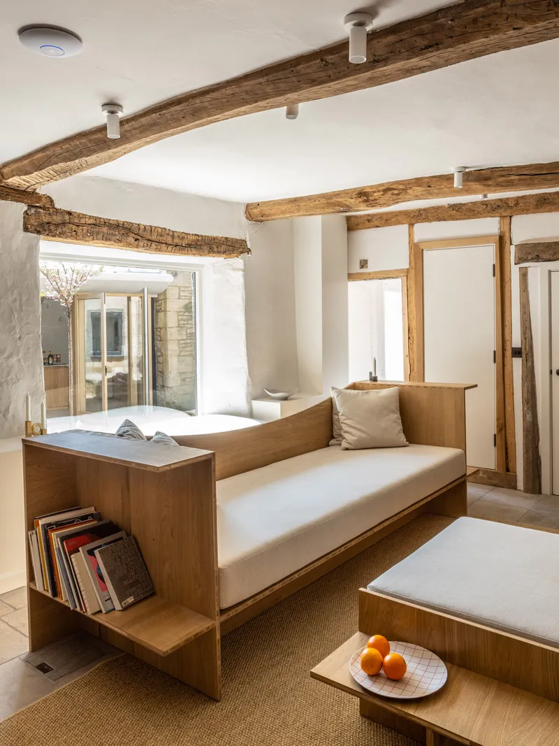 Built-in oak daybed with cushions and book storage under exposed ceiling beams facing glazed courtyard doors