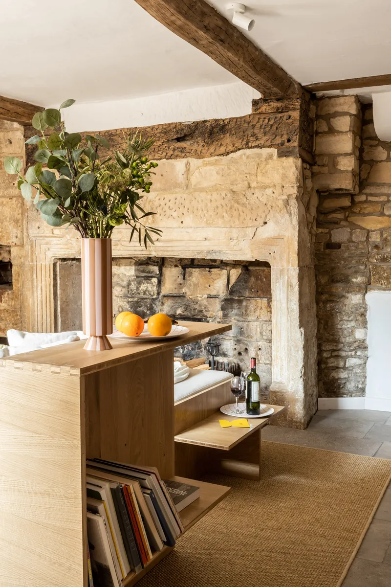 Interior view of a limestone fireplace surround beneath exposed timber beams with oak cabinetry