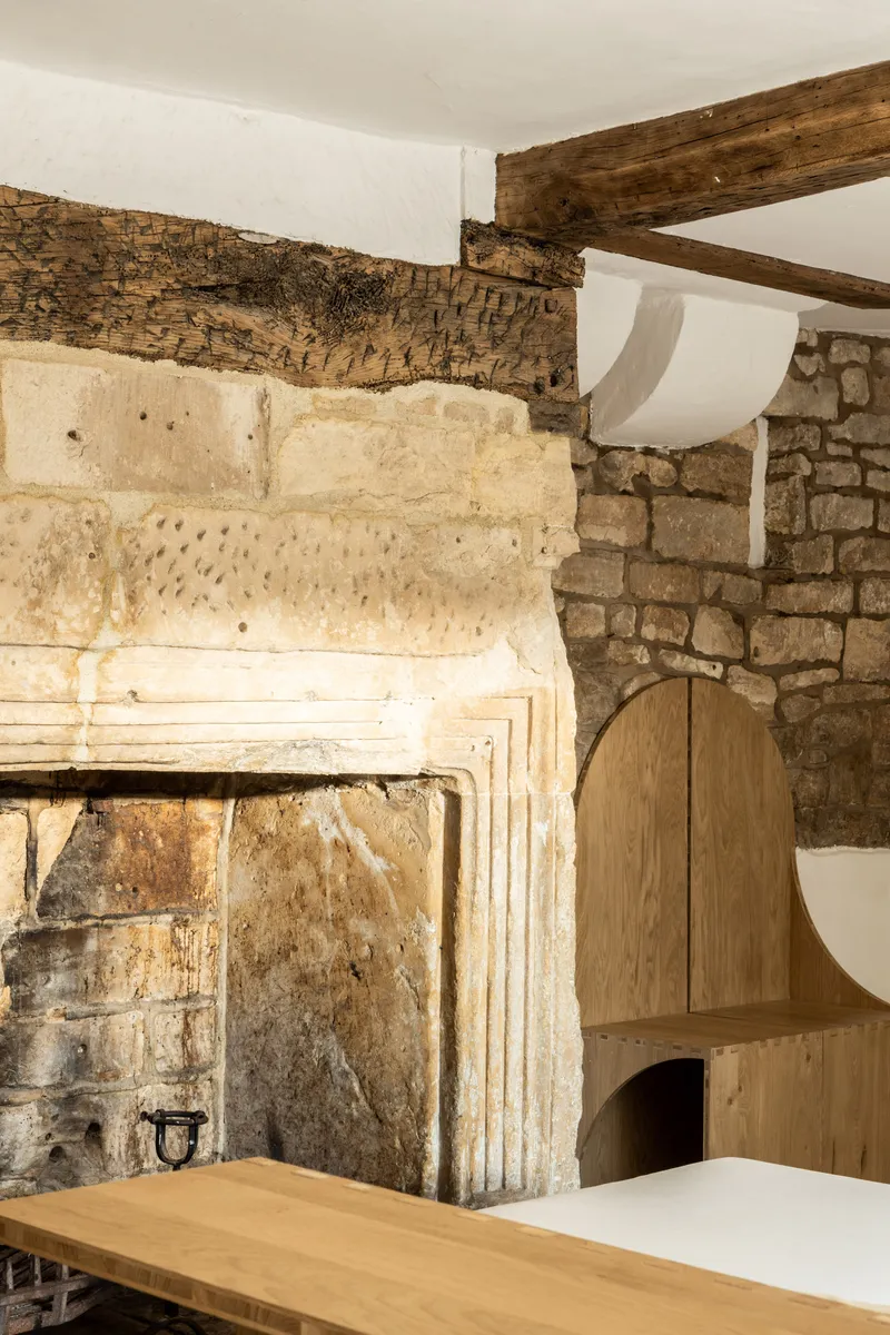 Carved limestone fireplace mantel with exposed timber ceiling joists and stone masonry wall