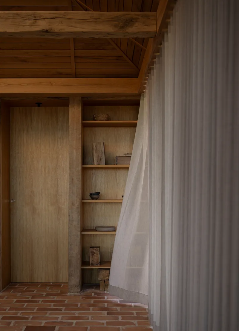 Interior alcove with plywood shelving and brick floor partially concealed by a linen curtain
