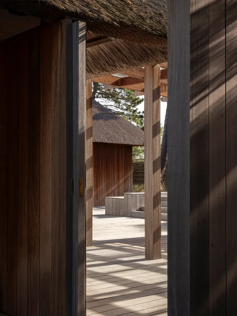 Timber columns framing a view through thatched pavilions with dappled sunlight on the deck