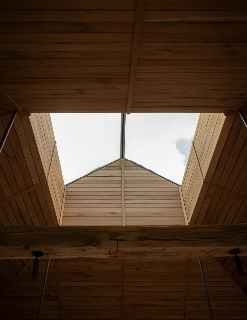 Upward view through a timber-lined skylight opening with exposed beams and pendant light