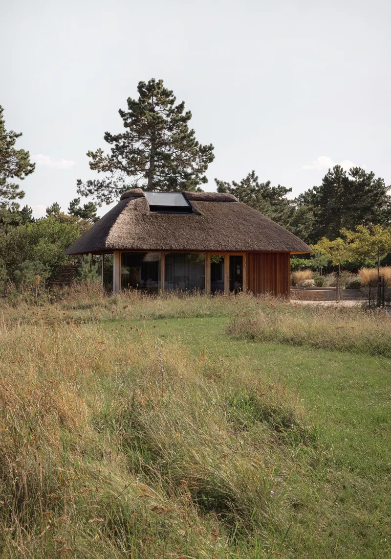 Circular thatched roof structure with vertical timber siding set in an open meadow landscape
