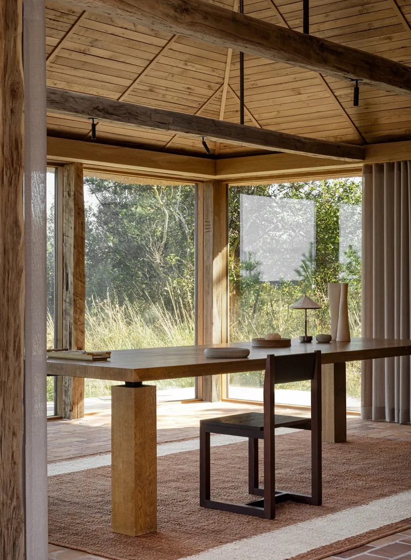 Interior dining space with exposed timber beams, planked ceiling and floor-to-ceiling windows overlooking grasses