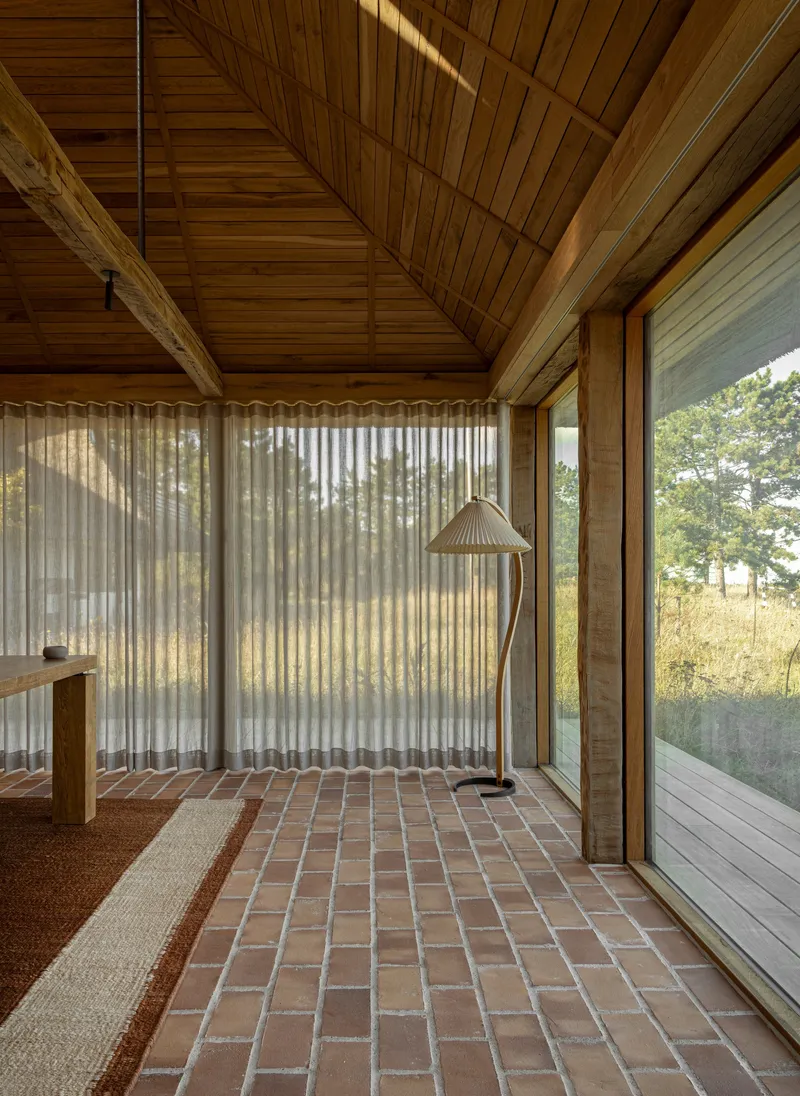 Brick paver floor meeting sheer curtains beneath a pitched timber ceiling in afternoon light